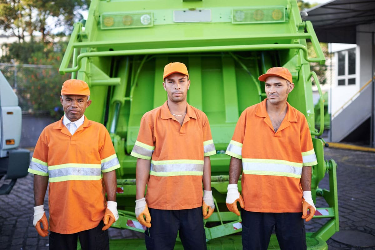 Municipal frontline workers (public sector) showing three council workers doing refuse collection standing in front of a garbage truck