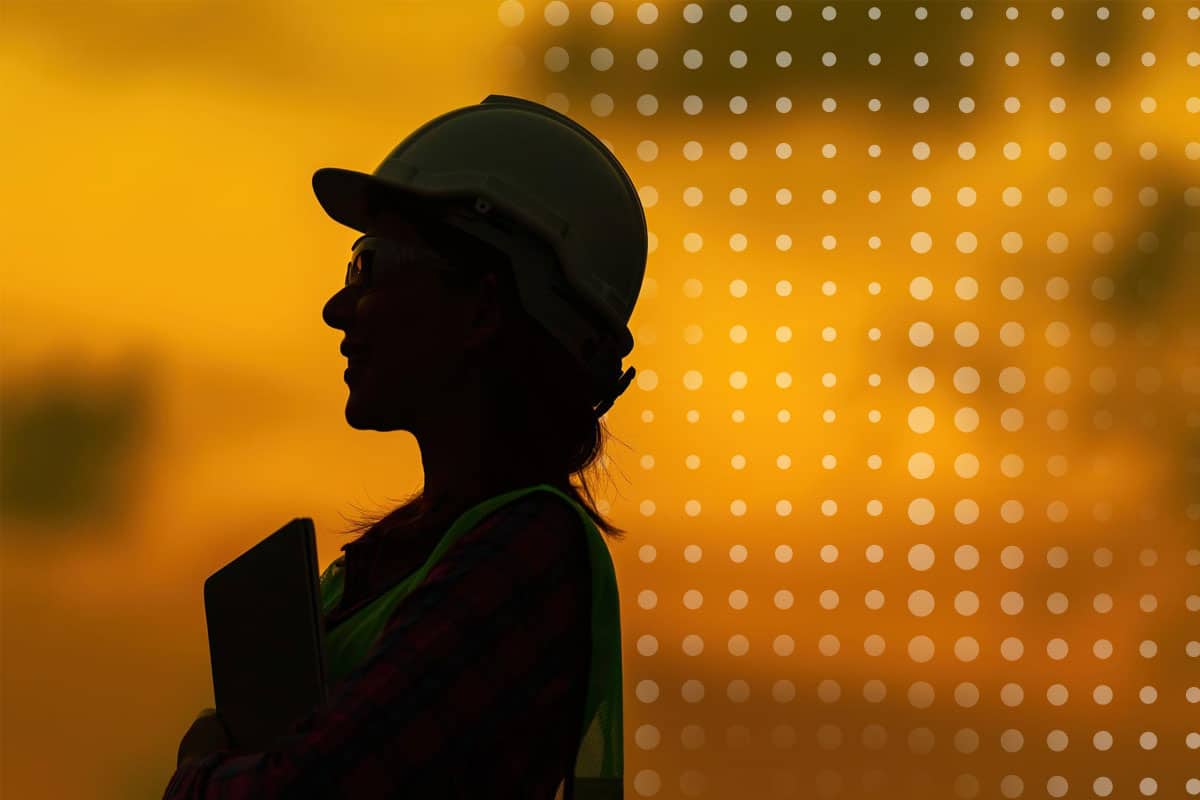 Female frontline worker wearing safety PPE silhouetted in the sunset/sunrise representative of in heavy industry sector